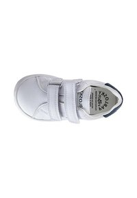 Zapatilla blanca para niños con dos correas de Velcro y una lengüeta azul marino en el talón, vista desde arriba sobre un fondo blanco.