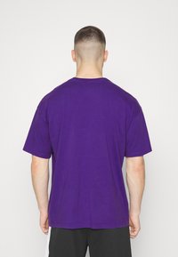 Camiseta de algodón morada con un corte relajado, mangas cortas y un cuello redondo acanalado. Sin logotipos ni patrones visibles.