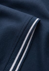 Nám̌ě modrý́ textil s texturovanou tkaninou, se bílými pruhy na okraji, ukazujícími čisté a precizní detaily stehu.