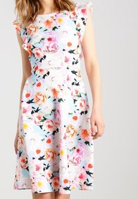 Blommig klänning med flerfärgade pionmönster på en ljus bakgrund. Volangärmar och A-linje-form med knälång kjol.