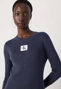 Marineblauwe geribbelde gebreide trui met een ronde hals en lange mouwen, voorzien van een wit Calvin Klein logo-patch op de voorkant.