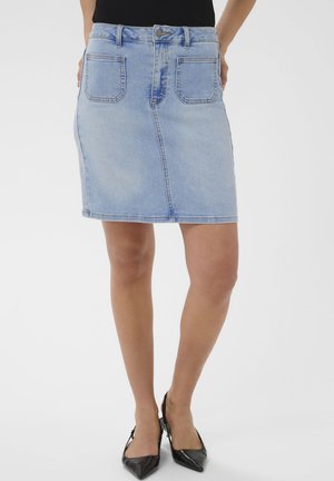 Gonna di jeans azzurro chiaro con tasche frontali, indossata con top nero e tacchi slingback neri con punta affilata su sfondo bianco.