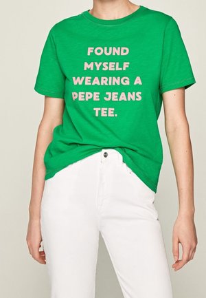 Vihreä lyhythihainen t-paita, jossa on vaaleanpunaista tekstiä: "FOUND MYSELF WEARING A PEPE JEANS TEE." Yhdistetty valkoisiin housuihin, yksinkertaisella designilla.