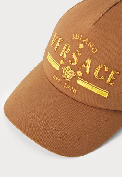 Căciulă maro din material textil, cu logo-ul galben brodat "VERSACE", un cap de leu și detalii "Milano EST. 1978" pe față.