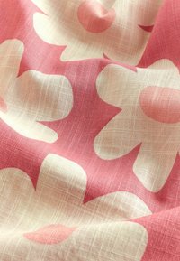 Vaaleanpunainen ja kerma värinen kukkakangas, jossa on suuria, abstrakteja kukkamuotoja, ja teksturoitu, pellavamainen kudonta.