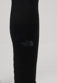 Leggings noirs avec un motif en nid d'abeille texturé, un design épuré et un logo discret "THE NORTH FACE" sur le bas de la jambe.