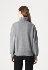 Pull à col roulé gris en maille douce. Présente une coupe ample, un col et un ourlet côtelés, avec des manches longues. Surface texturée.