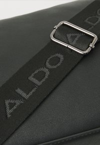Borsa in ecopelle nera con superficie testurizzata, ampia tracolla regolabile con logo "ALDO" e dettagli in metallo argentato.