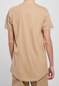 Beige tričko s krátkým rukávem, kulatým výstřihem, vyrobené z měkké bavlny. Má zakřivený lem a jednoduchou texturu, bez viditelných vzorů nebo akcentů.