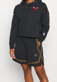 Sweat à capuche court noir avec logo des Bulls en rouge et poche avant. Associé à un short en mesh noir avec accents dorés et logo "FLY".