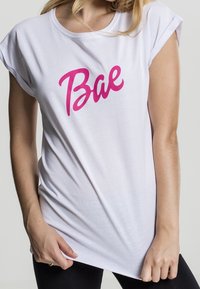 Witte t-shirt met korte mouwen, gemaakt van zacht materiaal, met grote roze "Bae" tekst op de voorkant, relaxte pasvorm en ronde halslijn.