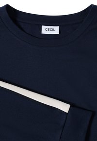 T-shirt bleu marine à manches courtes avec un col rond et une bande d'accent blanche. Le matériau semble lisse et léger. L'étiquette de la marque est visible.