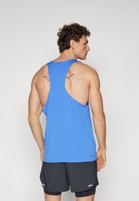 Top deportivo azul de tirantes con diseño de espalda nadadora, fabricado en material transpirable. Presenta un tejido texturizado y una etiqueta en el dobladillo. Short negro debajo.