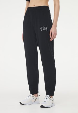 Pantaloni da jogging neri con cintura elastica, caratterizzati da un dettaglio ricamato bianco "TRN" sulla coscia sinistra e orli risvoltati.