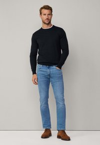 Czarny sweter, jasnoniebieskie dżinsy i brązowe skórzane buty. Sweter ma okrągły dekolt, dżinsy są dopasowane. Prosty, casualowy strój.