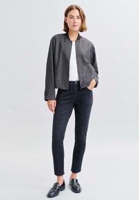 Grau bomberjacke mit strukturierter Oberfläche, schwarzer gerippter Kragen, getragen über einem weißen Hemd, kombiniert mit schmalen schwarzen Jeans und schwarzen Slippern.