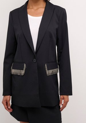 Sort enkelt-knaps blazer med sølvfringe på forlommerne, båret over en hvid top, vist fra skuldre til midt på låret.