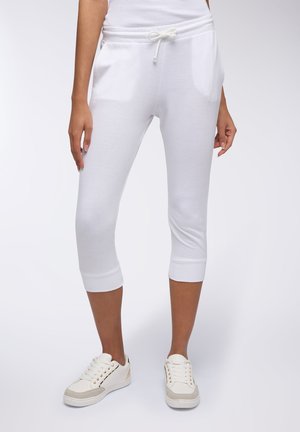 Pantaloni da tuta in cotone bianco a capri con vita elastica e cordino, tasche laterali e polsini a costine. Abbinati a sneaker bianche.