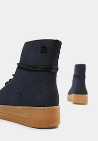 Sneakers alte navy in finta suede testurizzata, con lacci neri e suole in gomma. Presentano un logo impresso sul tallone.