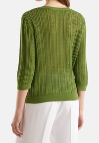 Grön stickad tröja med ett strukturerat mönster, med 3/4 ärmar och en rundad halslinning. Ribbad nederkant och muddar framhäver designen.