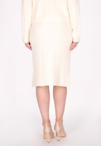 Cremfarbener Kabelstrickpullover und passender Rock. Der Stoff wirkt weich und hat ein strukturiertes Muster. Getragen mit hautfarbenen High Heels.
