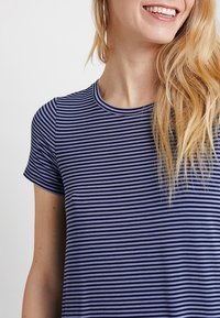 Pasiasty top z krótkim rękawem w kolorze granatowym i lawendowym. Posiada okrągły dekolt oraz miękką, gładką teksturę. Minimalistyczny design z klasycznym krojem.