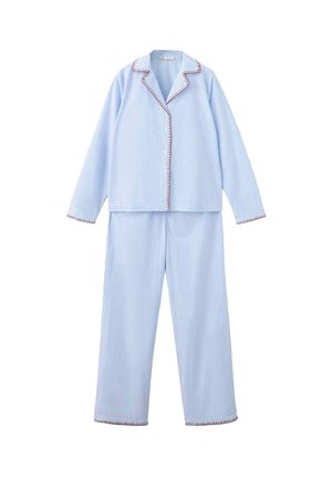 Woman standing barefoot wearing light blue striped long-sleeve pajama set with dark stitching on collar, cuffs, and hems against white background.