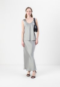 Hladký šedý bezrukávový top položený na odpovídající dlouhé sukni, doplněný černými slingback podpatky a malou černou kabelkou.