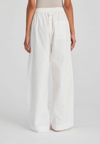 White wide-leg trousers with an elastic waistband, drawstring, and a single back pocket. Smooth texture and relaxed fit.