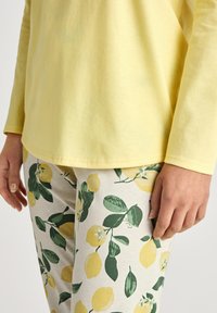 Gelbes Langarmoberteil kombiniert mit leichten Leggings aus Stoff, die ein Muster aus Zitronen und Blättern in Grün und Gelb zeigen.