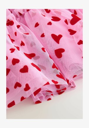 Rozā tilla audums ar maziem sarkaniem filca sirsniņām, ar mīkstu struktūru un kārtotām volānu kārtām, radot vieglu un gaisīgu izskatu.