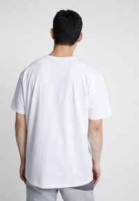 Maglietta in cotone bianco con vestibilità normale, maniche corte e scollo rotondo. Presenta una texture liscia e dettagli minimi.