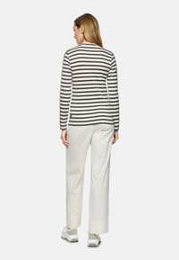 Gestreiftes Langarmshirt in Weiß und Braun mit einem runden Ausschnitt, kombiniert mit cremfarbigen, weitem Hosen und grauen Sneakern.