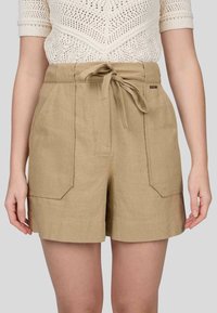 Shorts en lin beige à taille haute, avec ceinture à nouer et deux grandes poches avant. Dotés d'une texture lisse et d'un design ajusté.