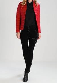 Röd vadderad jacka med quiltmönster, svarta texturerade byxor med dragkedjor och stora framfickor, samt svarta ankelboots.