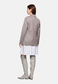 Gray pinstripe blazer with notch lapel, paired with a pleated white skirt and knee-high gray boots. Smooth fabric and tailored fit.