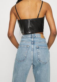 Czarny top z sztucznej skóry o kroju cropped z cienkimi ramiączkami, zestawiony z wysokimi, jasnoniebieskimi dżinsami, które mają duże tylne kieszenie oraz skórzaną metkę.