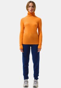 Oranger Rollkragenpullover aus weichem Strickstoff, kombiniert mit marineblauen Jogginghosen. Bequeme Passform mit langen Ärmeln und gerippten Bündchen.