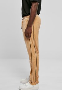 Fleece joggers in lichtbeige met zwarte zijstrepen, elastische tailleband en een tapered fit, gecombineerd met witte sneakers.
