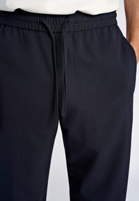 Pantalons de jogging navy avec taille élastique, cordon de serrage et poches latérales, présentant une texture lisse et un design fuselé.