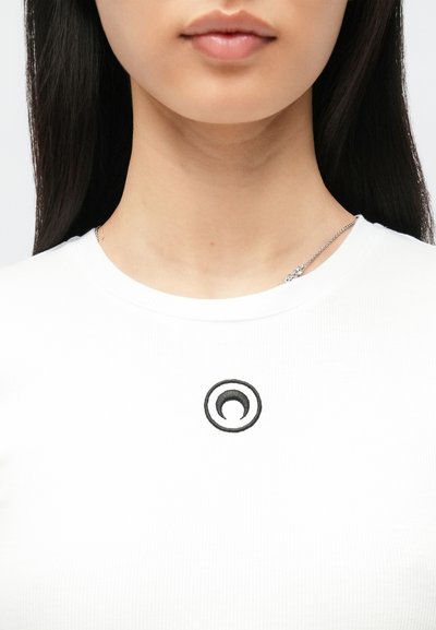 Biały prążkowany t-shirt z czarnym okrągłym haftem na środku. Gładka faktura tkaniny z okrągłym dekoltem.