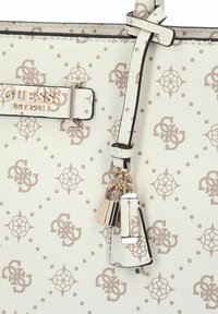 Witte gestructureerde handtas met beige logo met patroon en gouden accenten. Voorzien van een afneembare hanger en zwarte details. Klassiek ontwerp.