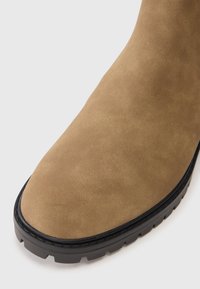 Barna suéd bokapuszta kerek orral, fekete gumitalppal és texturált felülettel. Tartós, kontrasztos fekete peremmel és mintázattal.