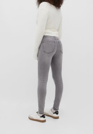 Šedé úzké džíny s vybledlým vzhledem, zadními kapsami a jemnými šitími detaily, doplněné bílými teniskami s černými akcenty.