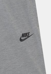 Grått tyg med en framträdande svart Nike-logotyp med swoosh, som visar en avslappnad kläddesign.
