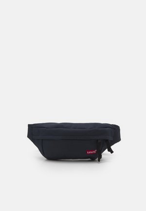 Sac banane compact noir Levi's avec poche zippée à l'avant et sangle réglable sur fond blanc.