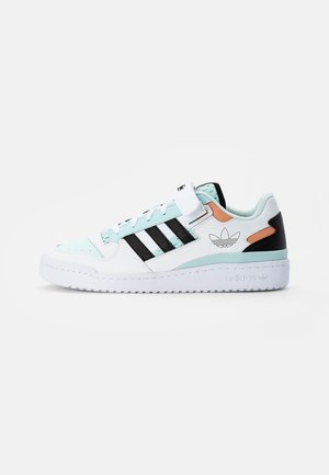 Baskets blanches Adidas avec des rayures noires, accents vert menthe, détails orange, lacets et bride en velcro, semelle en caoutchouc plate.