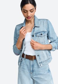 Giubbotto di jeans azzurro chiaro con bottoni argentati, due tasche sul petto e colletto classico, indossato sopra una canotta bianca e jeans azzurro chiaro.