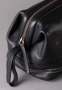 Black leather pouch with a textured surface, gold zipper, and white stitching. Features a handle for easy carrying and a rounded base.