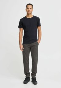 Zwarte katoenen T-shirt met ronde hals, gecombineerd met donkergrijze slim-fit broek en zwarte sportschoenen. Geen zichtbare patronen of accenten.